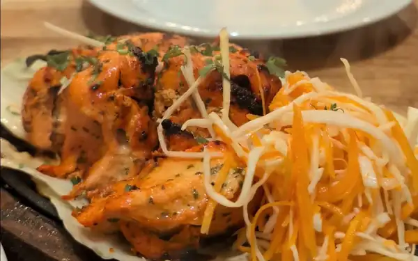 Grillowany kurczak z tandooru na drewnianej desce z marchewką i cebulą